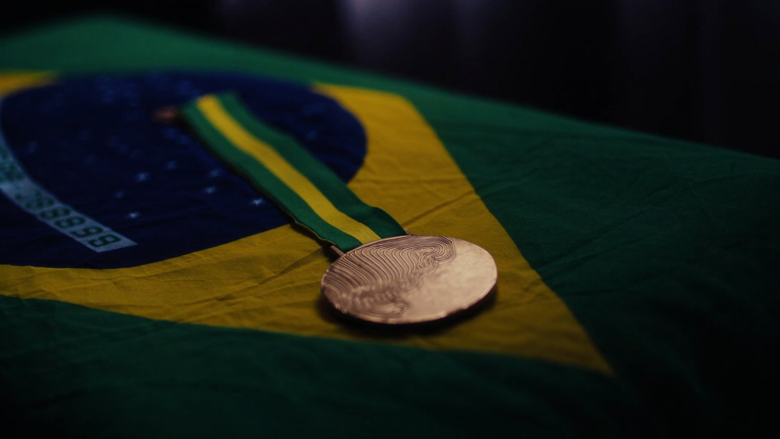 Medalha esportiva descansando sobre a bandeira do Brasil dobrada, iluminada em close editorial